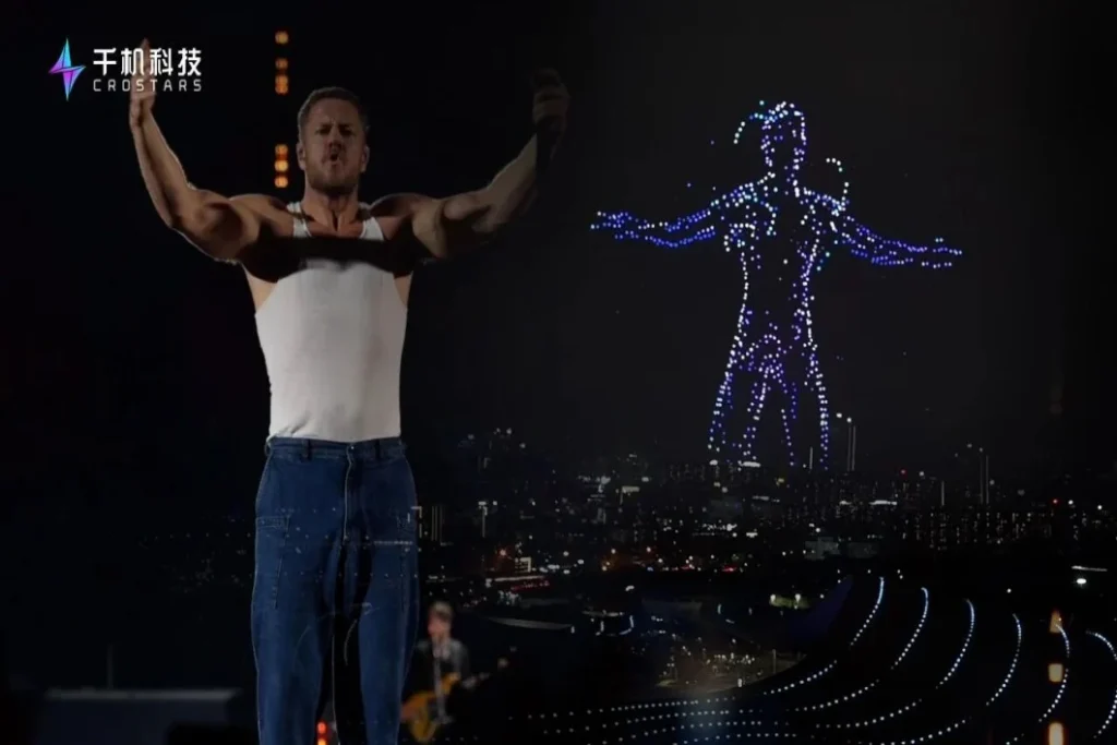 Crostars drone light show night performance, Guangdong Olympic Sports Center, Guangzhou, March 2026 — Dan Reynolds of Imagine Dragons performing on stage with drone formation visible in background