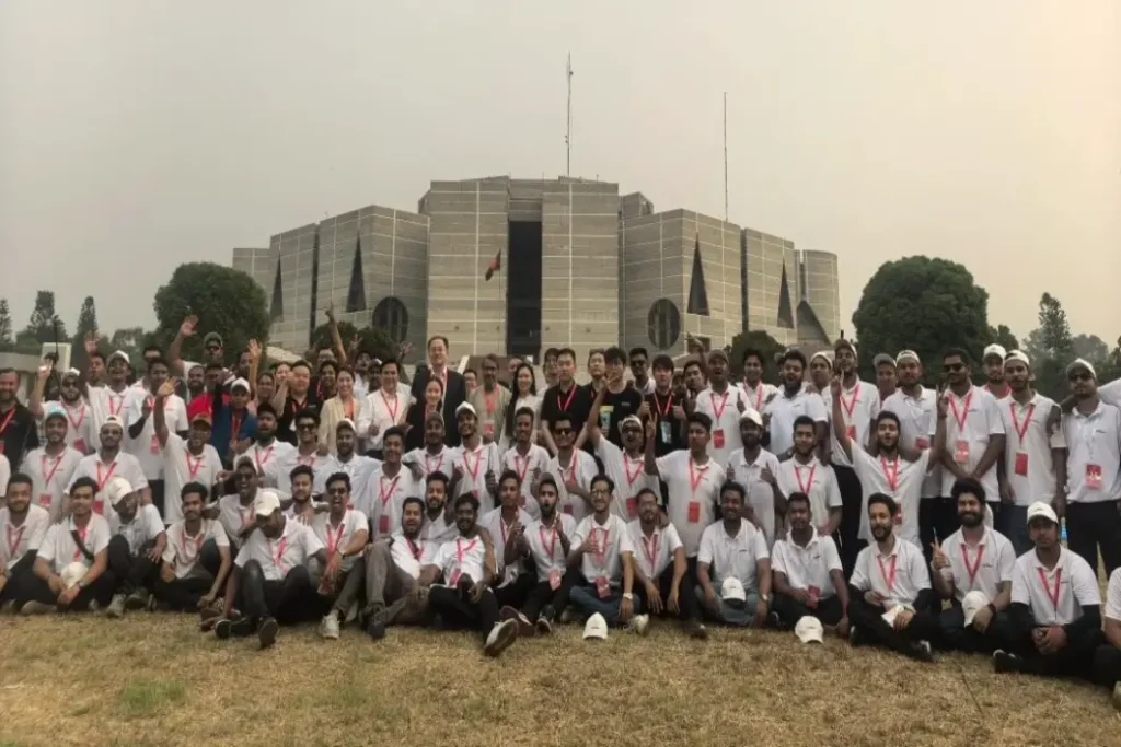 Crostars team and Bangladeshi ground crew in white shirts with red lanyards, group photo in front of Bangladesh National Parliament building, Dhaka, April 2025