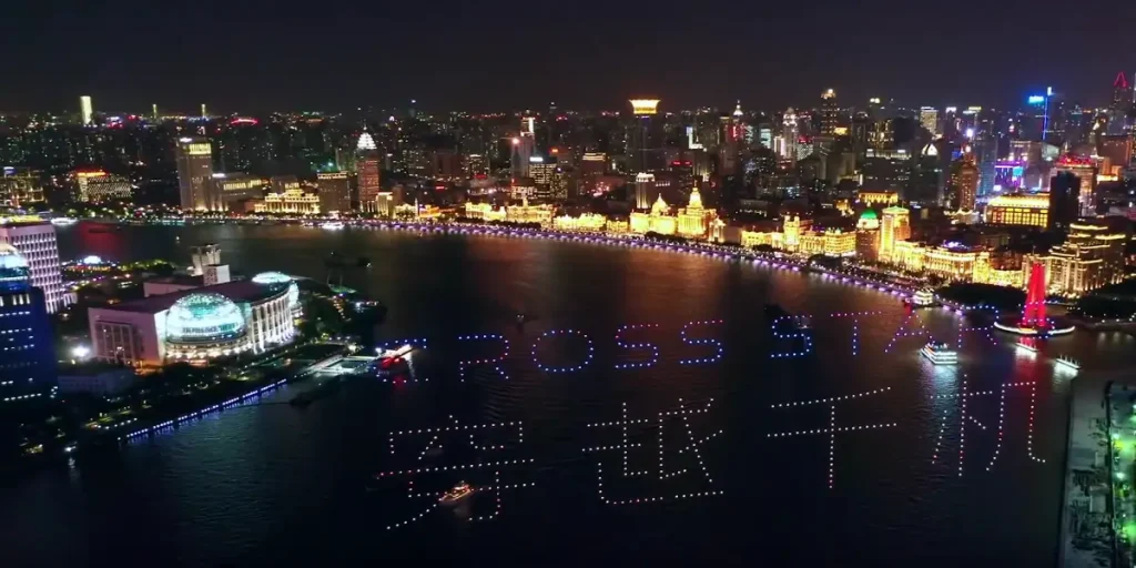 Crostars drone light show night performance aerial view over Huangpu River forming Crossstar and Chinese text, Shanghai Bund, 2020